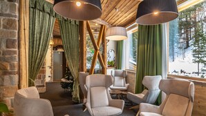 A cozy interior with wooden beams, green curtains, and multiple seating areas. - Hotel Garden (Andalo)