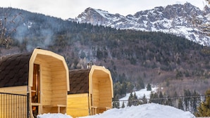 Two wooden cabins with sloped roofs, a wooden fence, and a snow-covered landscape with mountains in the background. - Hotel Garden (Andalo)