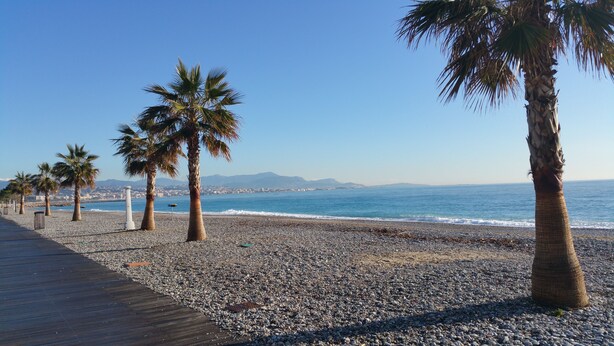 A pebble beach with palm trees and a wooden boardwalk leading to the sea. - 2-room apartment Résidence Provençale Air-conditioned Parking Pool 2 km Sea (Villeneuve-Loubet)