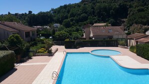 A swimming pool with a curved design, surrounded by a paved walkway and bordered by a low stone wall. - 2-room apartment Résidence Provençale Air-conditioned Parking Pool 2 km Sea (Villeneuve-Loubet)