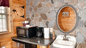 Une cuisine compacte avec un mur en pierre, un plafond en bois, un four à micro-ondes, une machine à café, un évier et une poubelle.