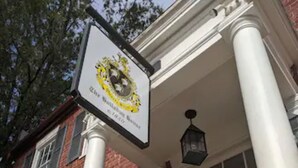 A building with a blue door, a black balcony with flowers, and a sign with a yellow emblem. - The Arundel Room in historic Holladay House (Orange)