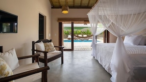Ein Schlafzimmer mit Bett, Sessel, Fernseher und Blick auf Pool und Außenbereich.