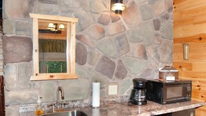 A compact kitchen with a stone wall, wooden cabinets, a sink, a coffee maker, a microwave, and a trash can. - 1/2 double cabin with king bed and single child sized pull-out sleep sofa (sleeps 2 adults & 1 child (Flintstone)