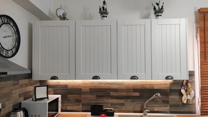 Una cocina moderna con armarios blancos, encimera de madera, microondas integrado, hervidor y una vela roja.