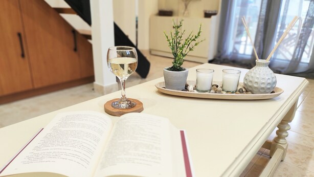 Un libro abierto sobre una mesa, con una copa de vino blanco, una pequeña planta en maceta y tres velas.