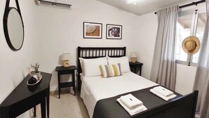 Habitación de hotel ordenada con cama, mesitas de noche, un espejo y dos cuadros en la pared.