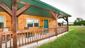 A log cabin with a porch, wooden chairs, and a green door. - 1/2 of a double cabin with two queen beds (sleeps 4). (Flintstone)