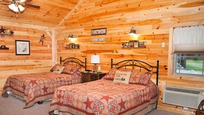 A cabin-style room with two beds, wooden walls, a ceiling fan, a window with curtains, and a small table with a lamp. - 1/2 of a double cabin with two queen beds (sleeps 4). (Flintstone)