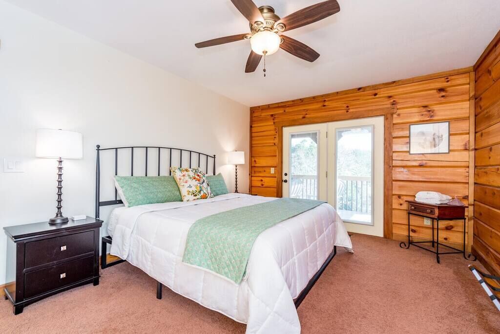 Une chambre à coucher avec un lit, des tables de chevet, un ventilateur de plafond et une fenêtre.