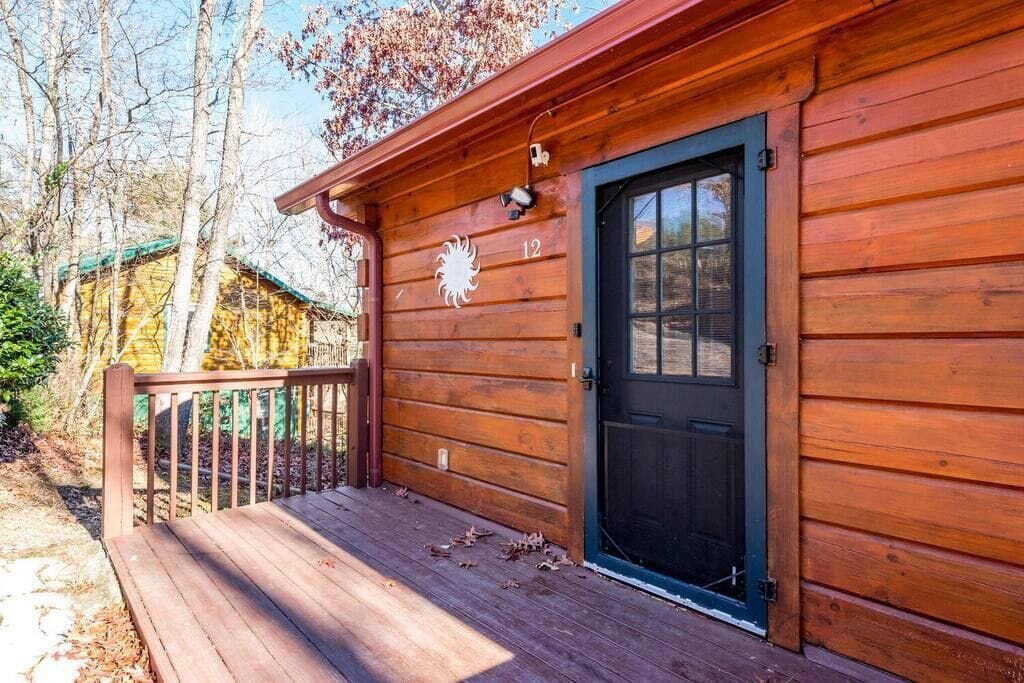 A wooden cabin with a black door, a deck, and a number '12' sign.