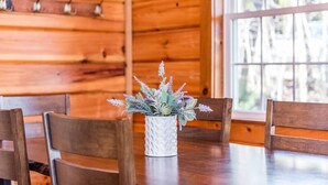 Ein Holzespeisesaal mit einer weißen, strukturierten Vase, die eine Pflanze enthält, umgeben von Holzstühlen, in einem Raum mit Holzwänden und einem großen Fenster.