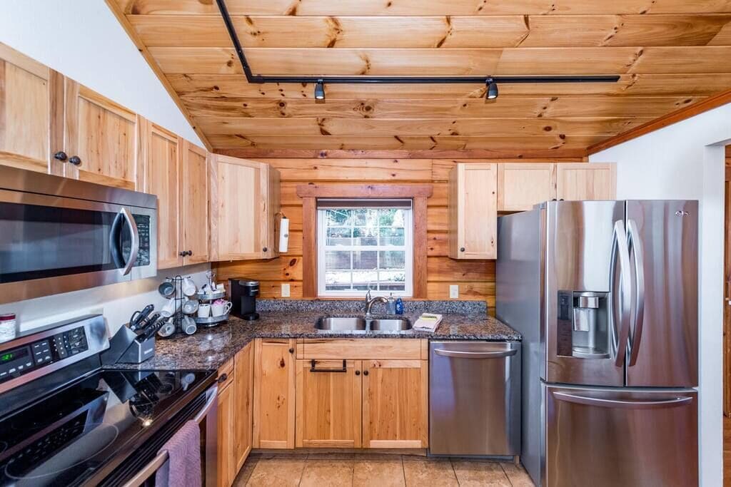 A modern kitchen with wooden cabinets, stainless steel appliances, granite countertops, and a window providing natural light.