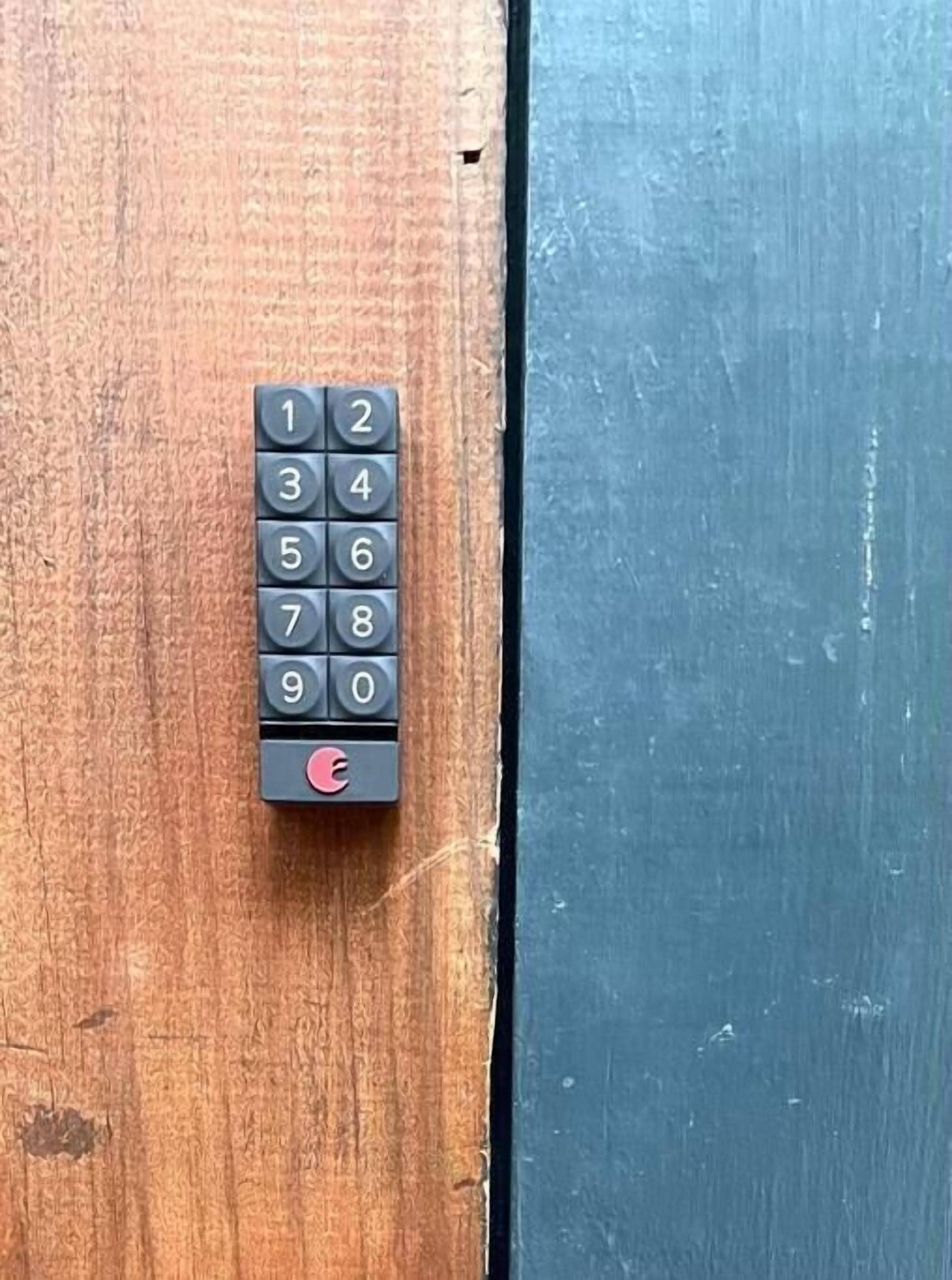 Una serratura con tastierino su una porta in legno, con una superficie blu adiacente.