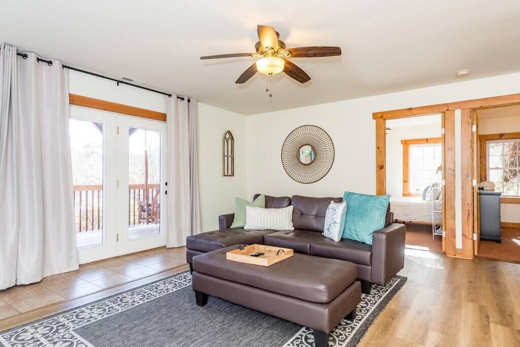 A spacious living room with a brown leather sofa, a ceiling fan, and a large mirror on the wall.