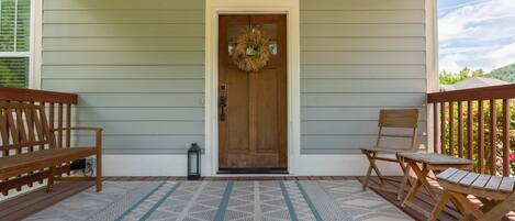 A porch with a wooden door, two wooden benches, and a patterned rug.