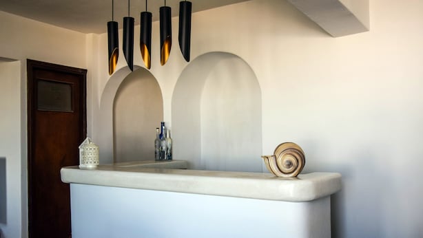 Una zona d'acollida amb un taulell blanc, una porta de fusta i tres llums penjants.