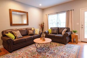 A living room with two brown leather sofas, a round coffee table, a large mirror, and a patterned rug.
