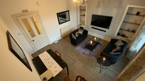Una sala de estar moderna con un televisor de pantalla plana, una araña y un comedor con mesa y sillas.
