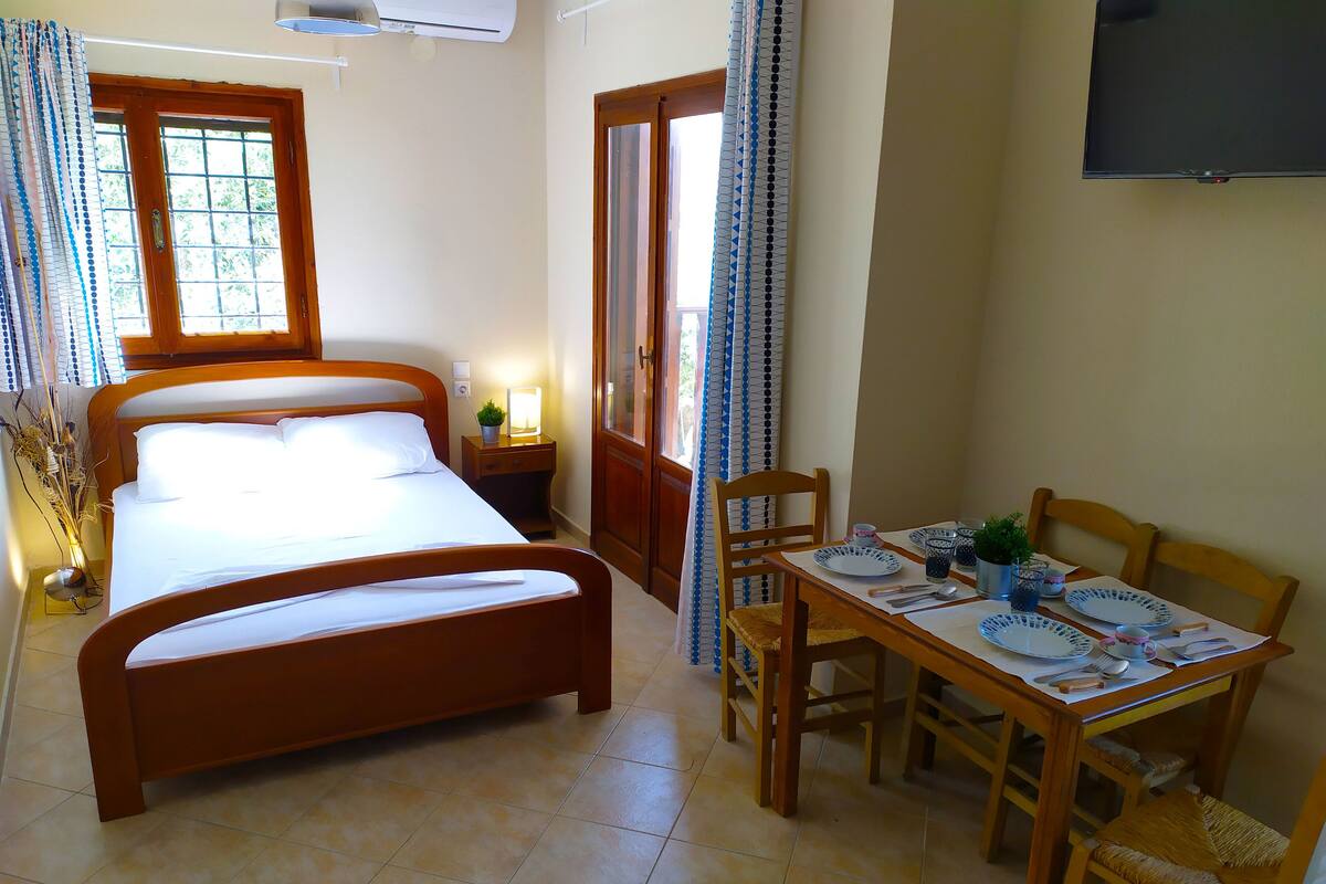 Un dormitorio con cama, mesita de noche, lámpara y una zona de comedor con mesa, sillas y platos.