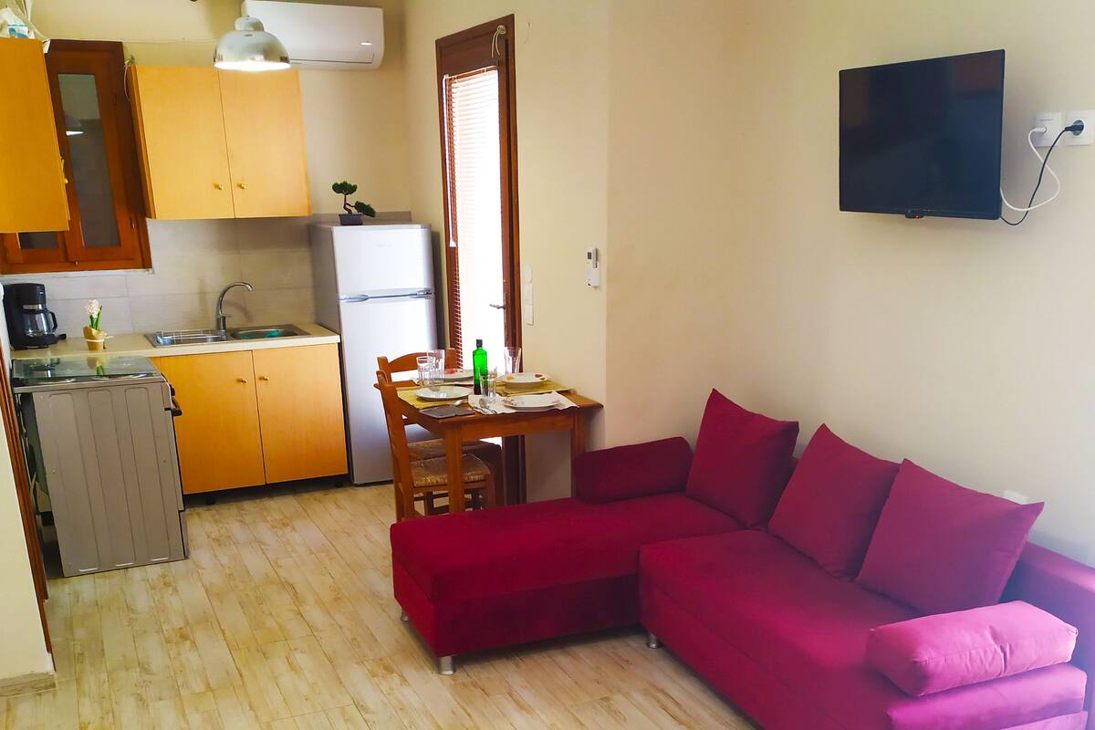 Un espacio habitable compacto con kitchenette, comedor y sofá rojo.