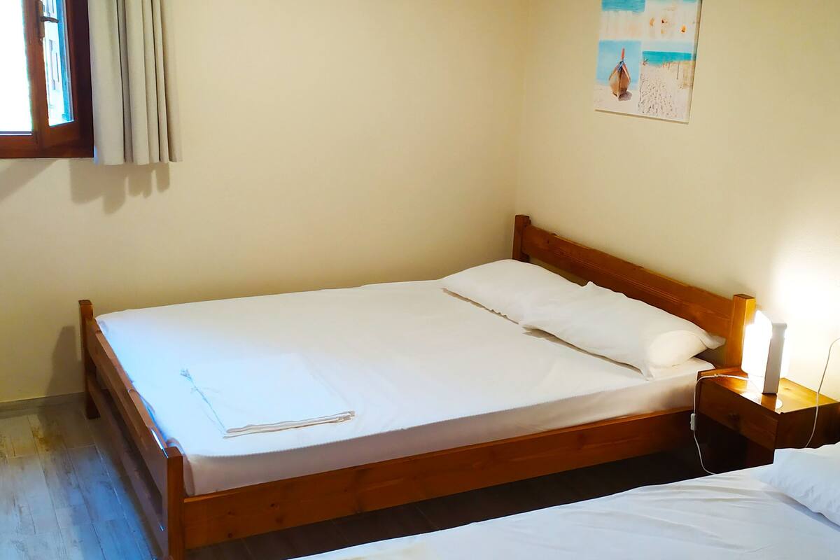 Una cama individual con estructura de madera, una mesita de noche con una lámpara y un cuadro en la pared.
