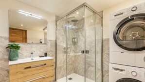Un baño moderno con ducha acristalada, lavadora Bosch y tocador de madera con cajones.