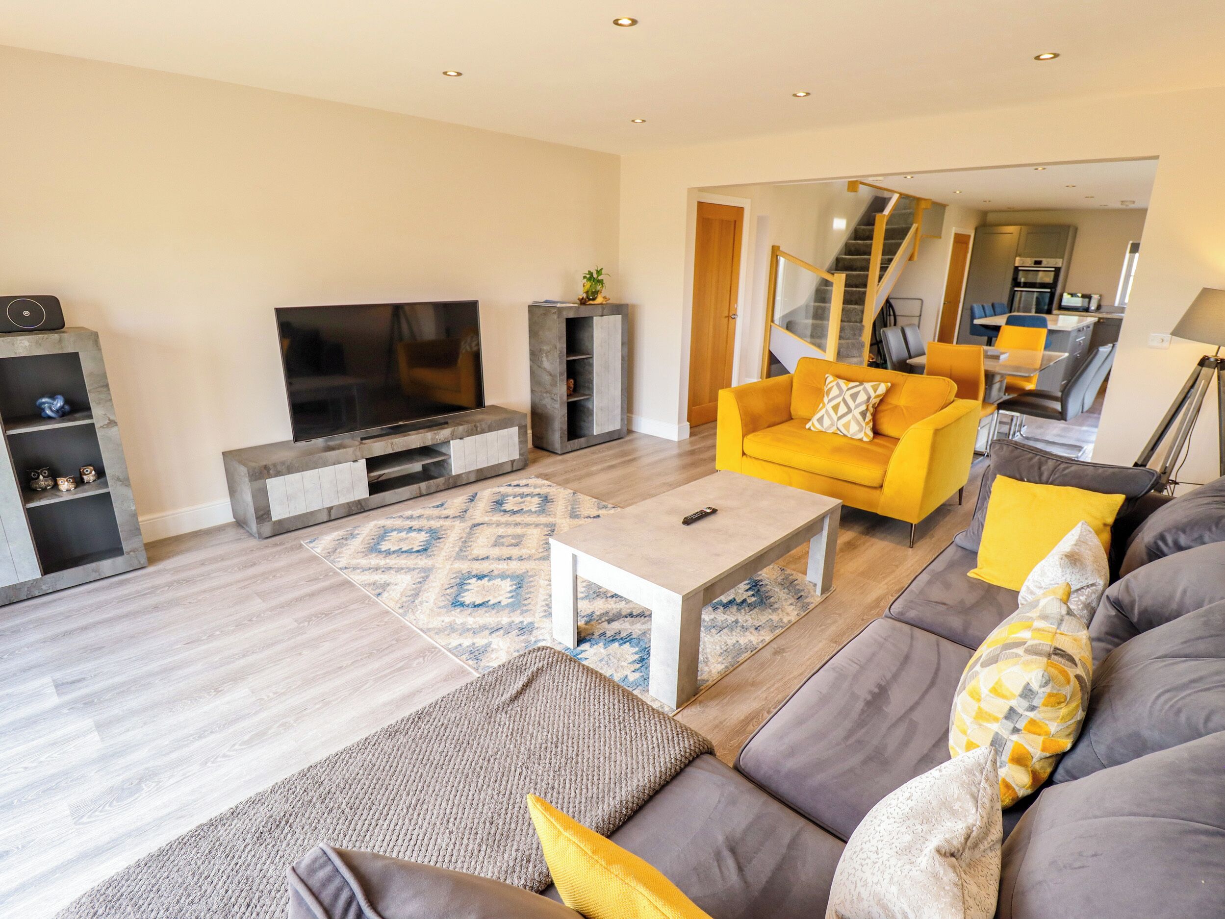 A modern living room with a flat-screen TV, a sofa, a coffee table, and a staircase leading to an upper floor.