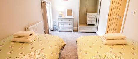 A bedroom with two beds, a dresser, a mirror, and a wardrobe.