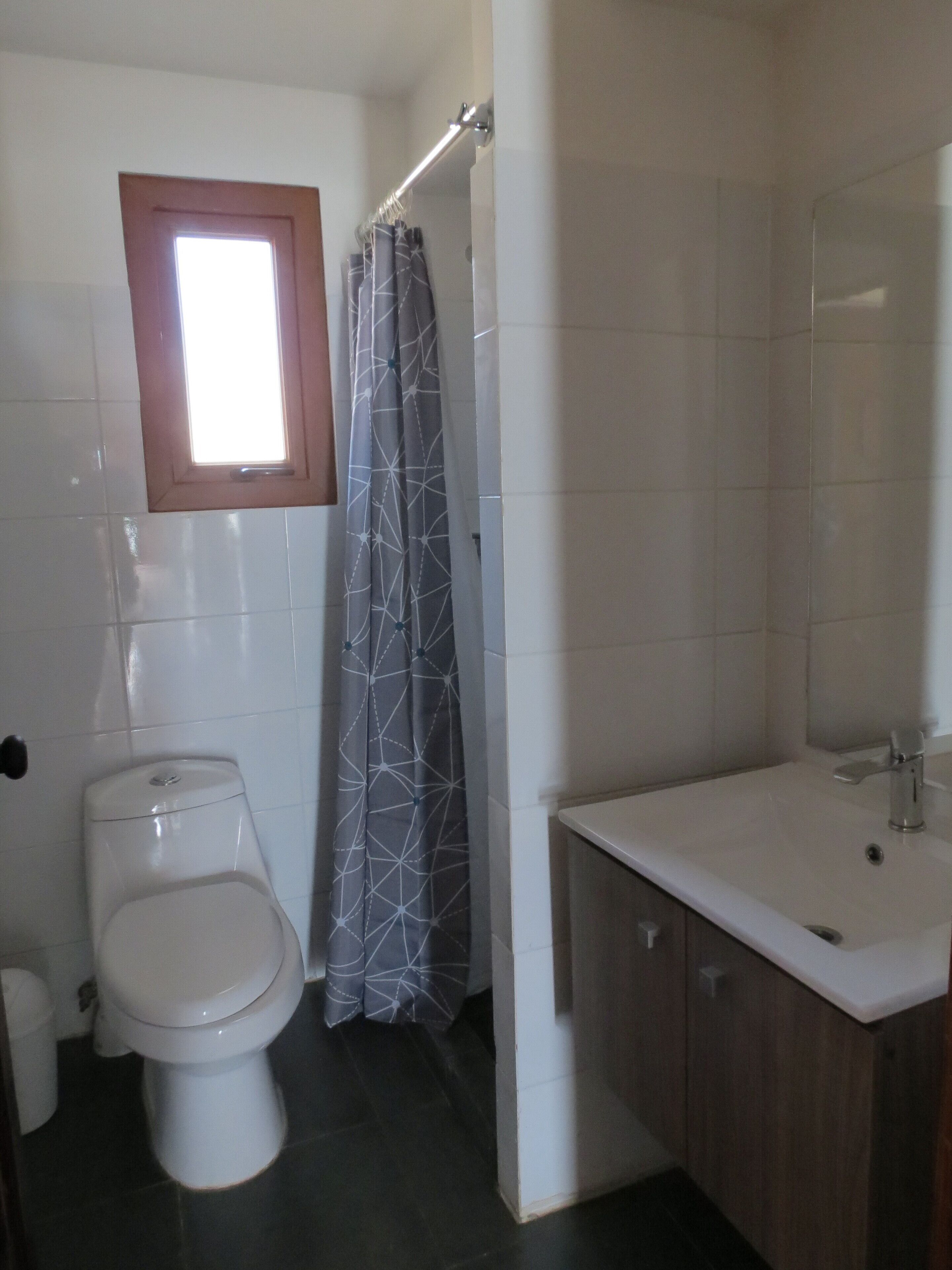 A bathroom with a toilet, a shower with a patterned curtain, and a sink with a wooden cabinet.