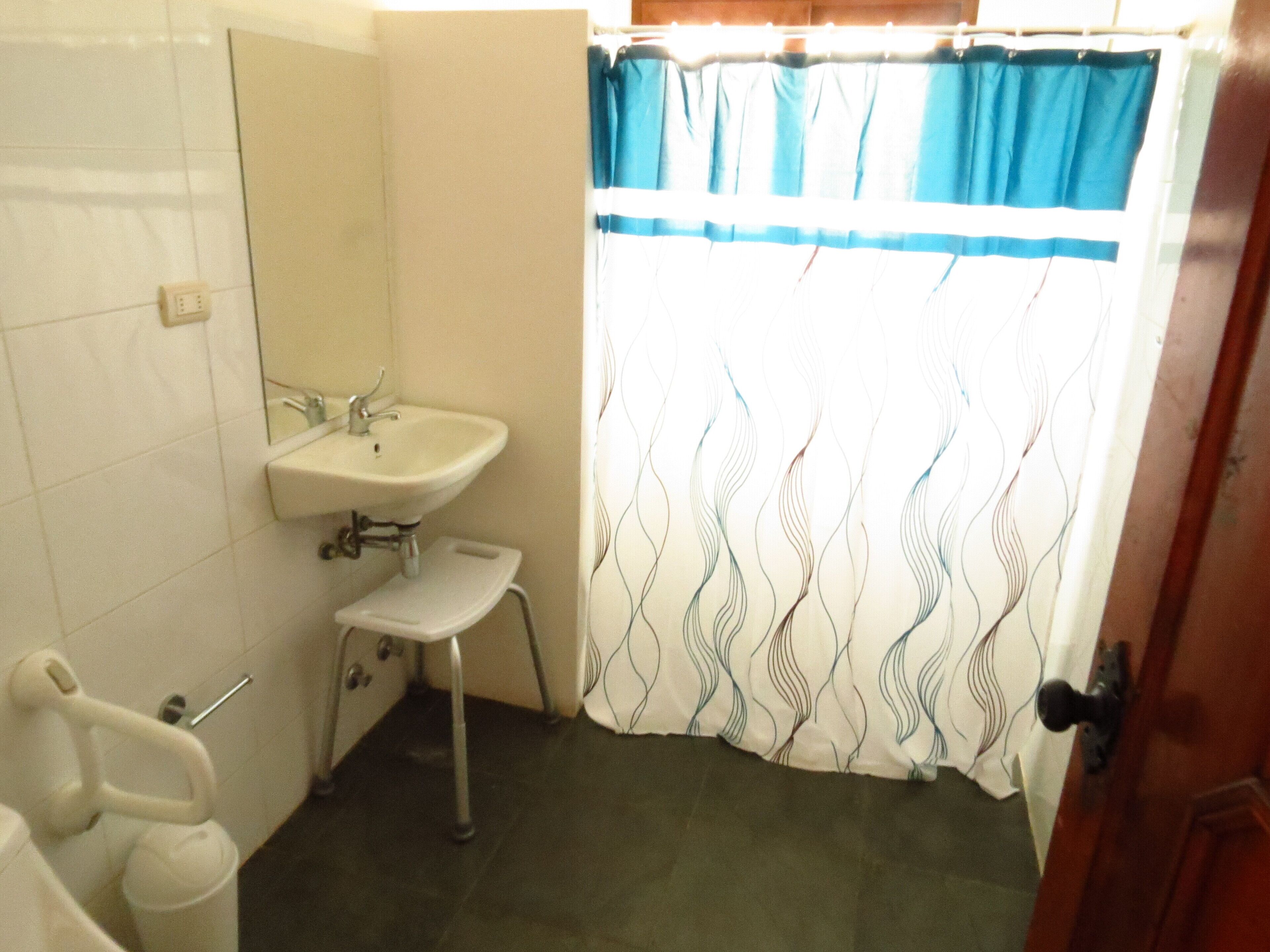 Baño con lavabo, espejo y taburete accesible para sillas de ruedas.