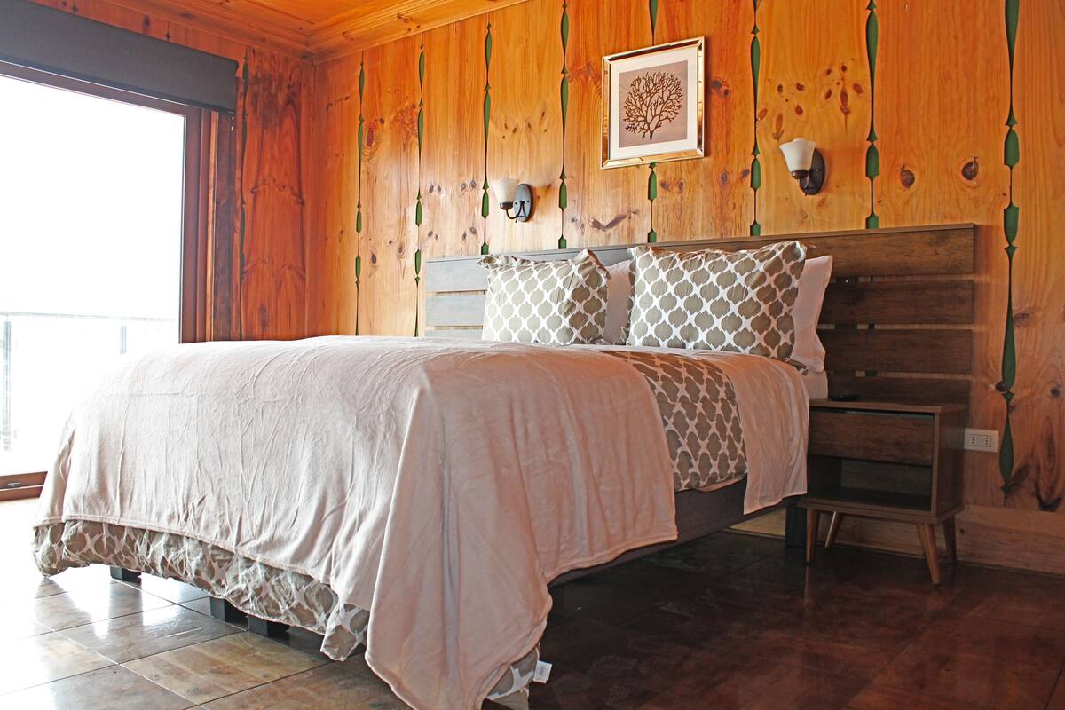 A wooden-paneled bedroom with a bed, a nightstand, and a framed picture on the wall.