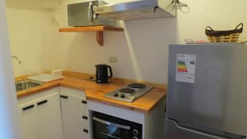 Une cuisine compacte équipée d’un four encastré, d’un four à micro-ondes, d’une bouilloire et d’un réfrigérateur.