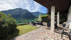 Un patio con suelo de piedra, mobiliario exterior y vistas a un lago y montañas.