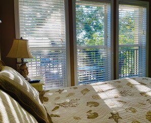 Relax in this serene bedroom with a large bed, featuring a leaf-patterned quilt, and enjoy the view of lush greenery outside through the windows.