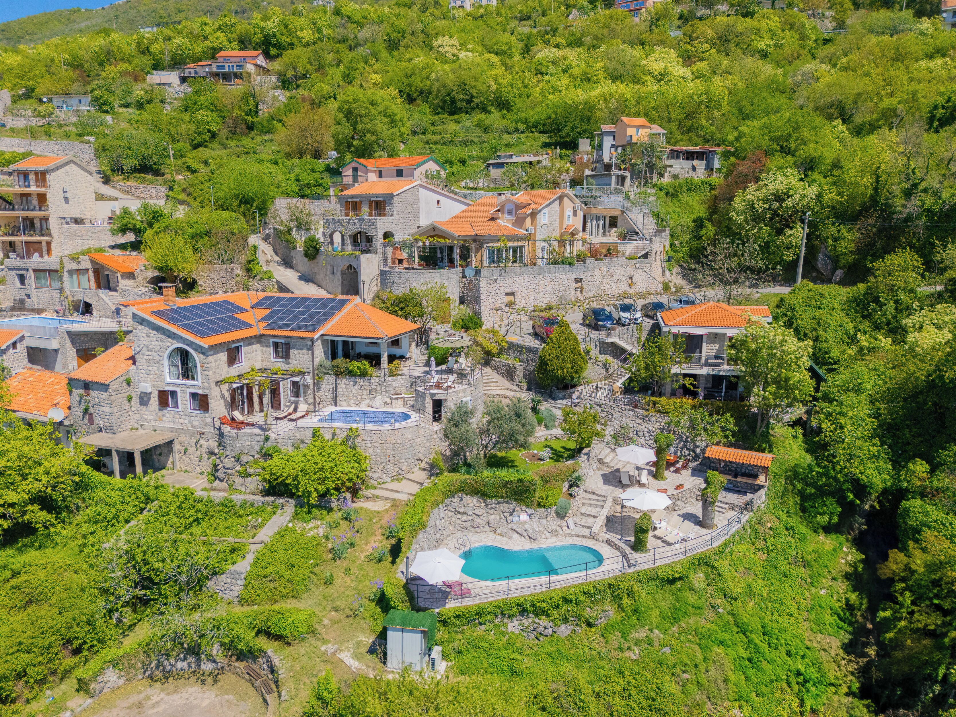 Un quartier résidentiel situé sur une colline, avec des maisons en pierre, une piscine et des panneaux solaires.