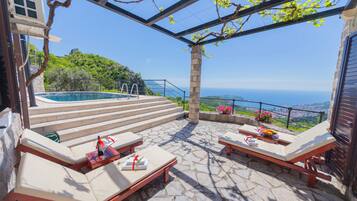 Une terrasse sur le toit avec un sol en pierre, des chaises longues, une petite piscine et une vue sur la mer.