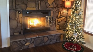 A stone fireplace with a lit fire, a Christmas tree with lights, and a cozy rug. - Charming cozy lake cabin, 300 yds from Lake Texoma beach, fishing, boat ramp! (Pottsboro)