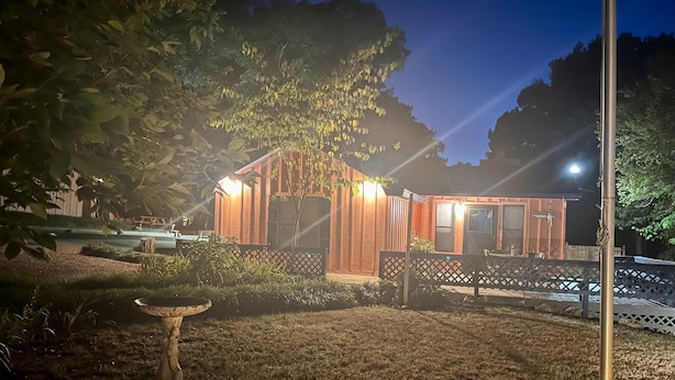 A rustic wooden cabin with a sloped roof, surrounded by a wooden fence and a garden area with a birdbath. - Charming cozy lake cabin, 300 yds from Lake Texoma beach, fishing, boat ramp! (Pottsboro)