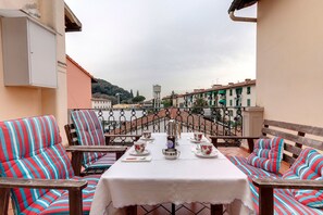 A terrace with a table set for tea, striped chairs, and a view of a bridge and buildings.