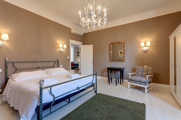 A bedroom with a bed, a chair, a mirror, and a chandelier.
