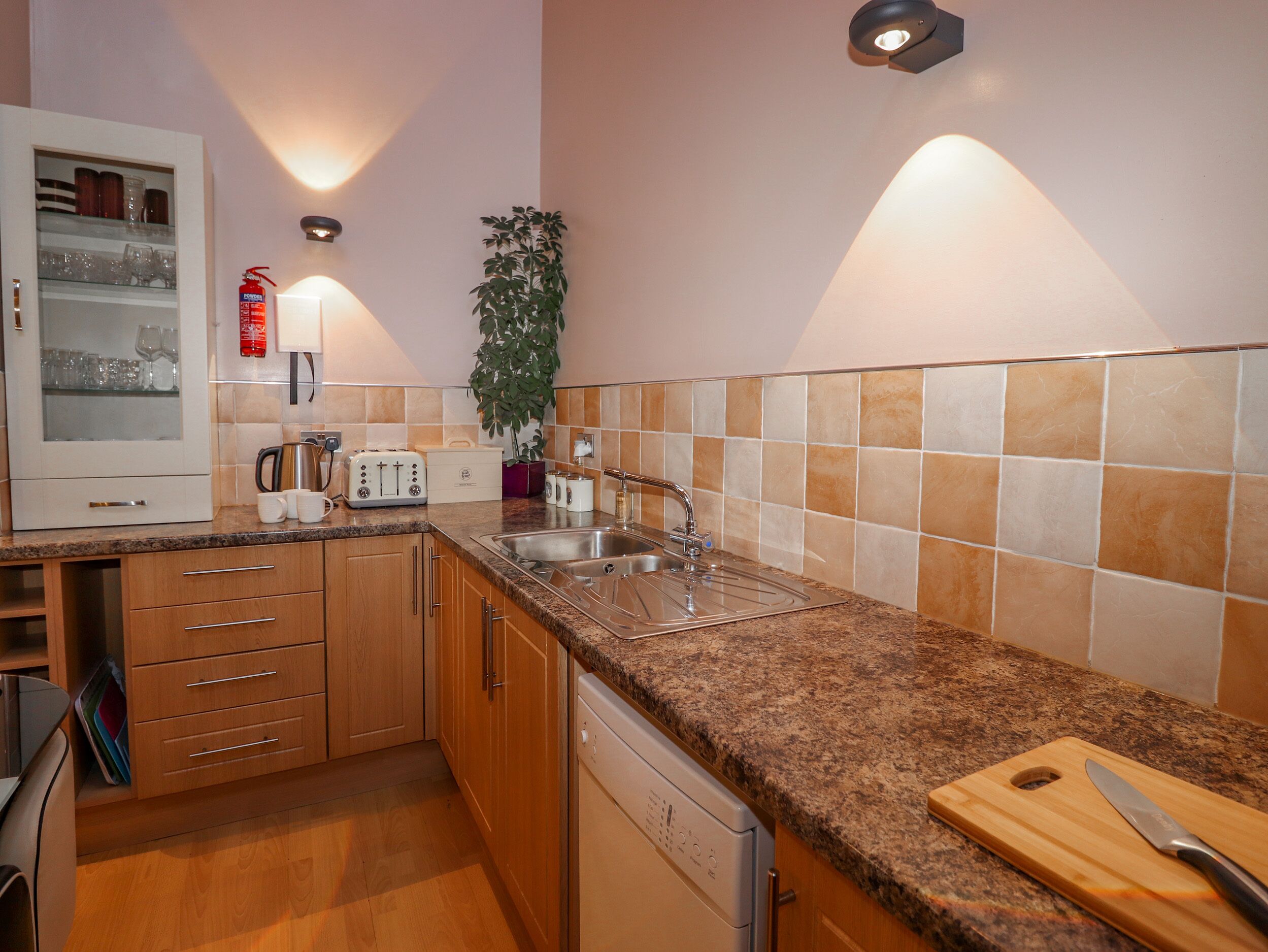 Una cocina moderna con armarios de madera, encimera de granito, lavavajillas integrado y un tostador.
