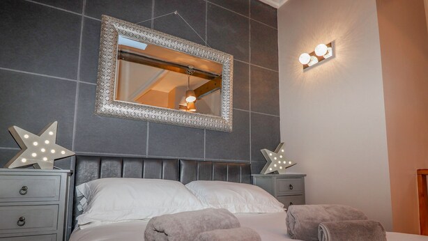 A neatly made bed with two pillows and two rolled towels, a headboard with a mirror, and two bedside tables with star-shaped light fixtures.