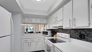 A modern kitchen with white cabinets, a microwave, an oven, and a black backsplash. - Oceanfront walkout stunning condo! (Cape Canaveral)