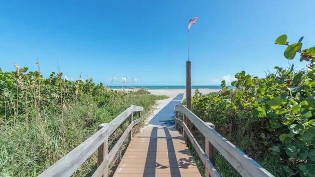 A wooden boardwalk leading to a beach with an American flag on a pole. - Oceanfront walkout stunning condo! (Cape Canaveral)