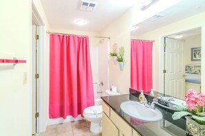 Bathroom features a large mirror, white sink, toilet, and shower area with a curtain.