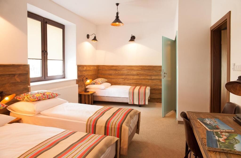 Une chambre confortable avec deux lits, une tête de lit en bois, une petite table de chevet avec une lampe, et une vue sur une porte verte.