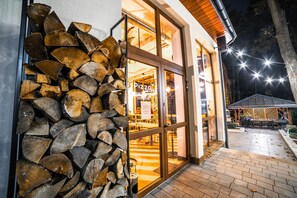 A restaurant with a stone wall of firewood, large glass doors, and outdoor seating visible through the windows. - Hotel Montis (Poniatowa)