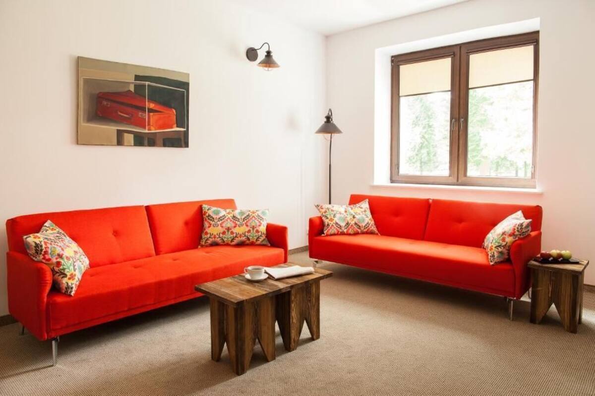 A room with two red sofas, a wooden coffee table, a lamp, a painting, and a window with a view of greenery.