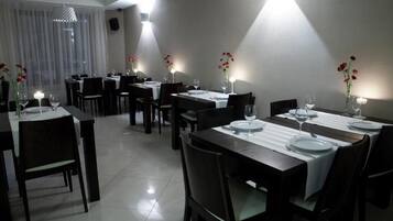 A dining area with multiple tables set for dining, each with white tablecloths and candles.